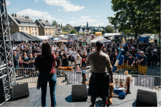 Blick von der Bühne auf die zahlreichen Besucher*innen des Festivals; im Vordergrund Redner und Gebärdendolmetscherin