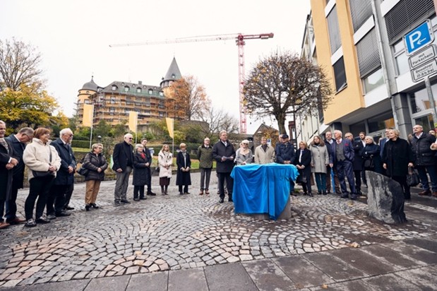 Eine Gruppe von mehr als 30 Personen wartet gespannt am noch verhüllten Modell